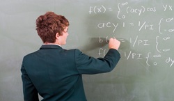 Secondary school pupils writing maths sums on blackboard
