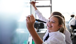 Two secondary school pupils smiling and writing on whiteboard
